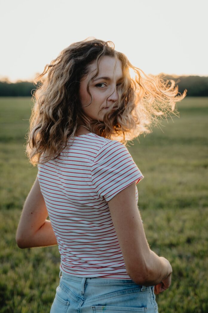 Photo by Drew Hays Woman with curly hair in a field at sunset