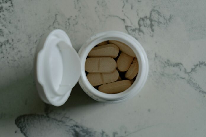 Opened bottle of beige pills on marbled surface